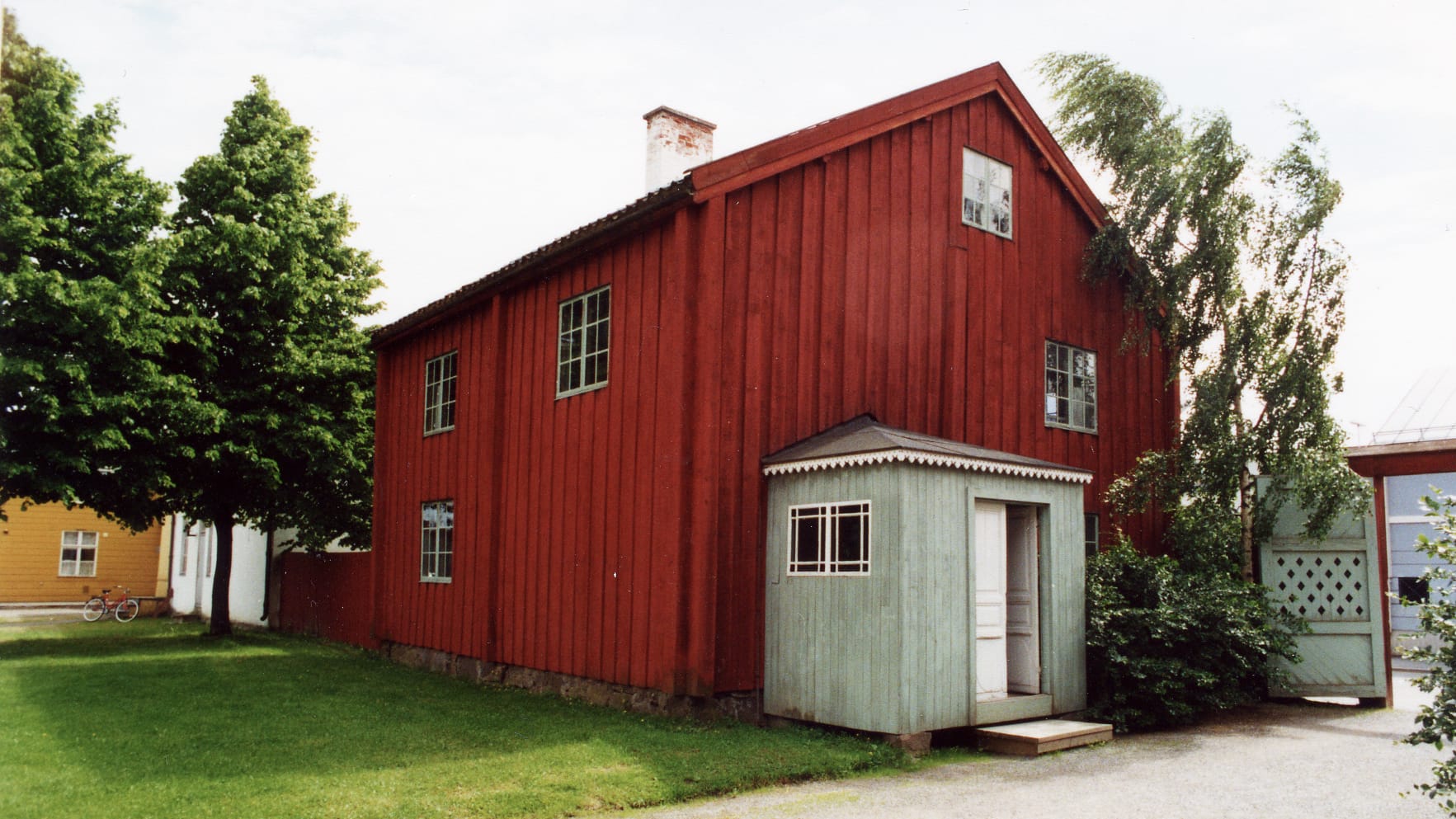 Punainen, puinen vanha rakennus kesällä kuvattuna.