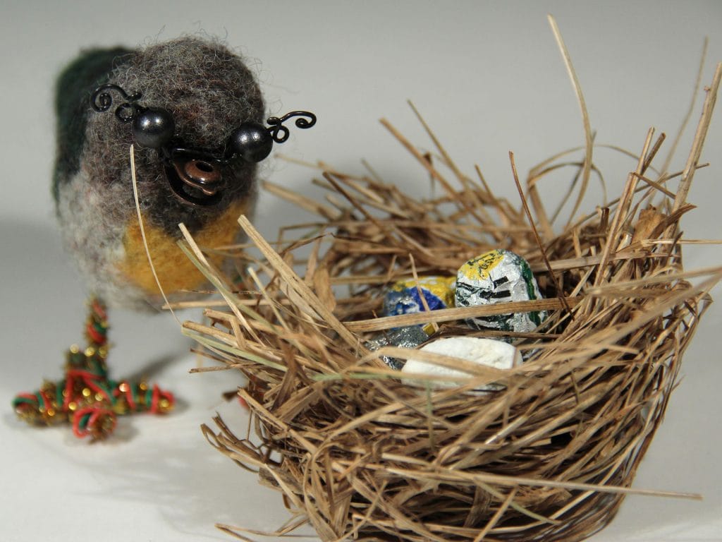A bird, a bird nest and eggs made of different materials.