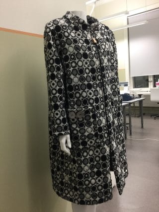 Mustavalkoisesta villakankaasta tehty polvipituinen takki.