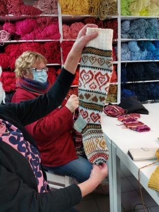 Etualalla nainen esittelee neulomiaan kirjoneulevillasukkia, taka-alalla erivärisiä neulelankoja.