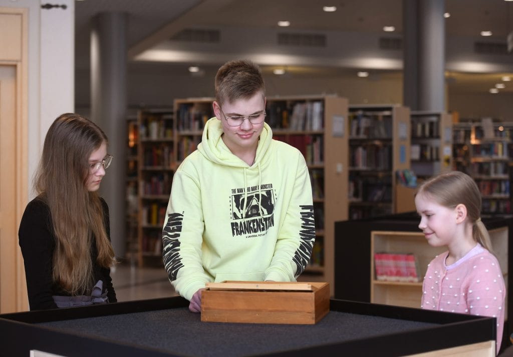 Kolme nuorta seisoo pöydän ympärillä ja pelaa Labyrintti-peliä.