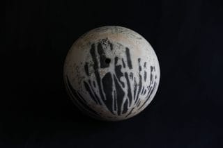 A black-white-brown ball made of clay with a small hole.